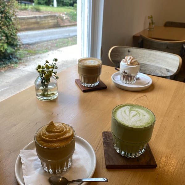 Four healthy drinks and desserts on a wooden table by a window at Good Kitchen.