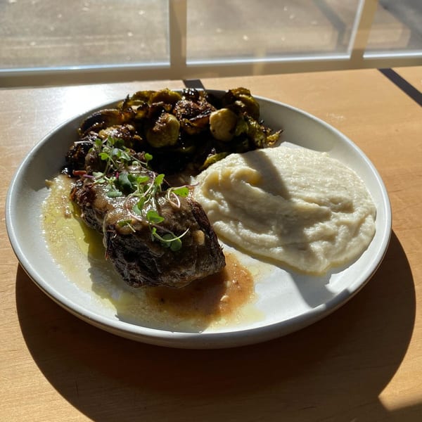 Braised short ribs with mashed cauliflower and roasted Brussels sprouts on a white plate.