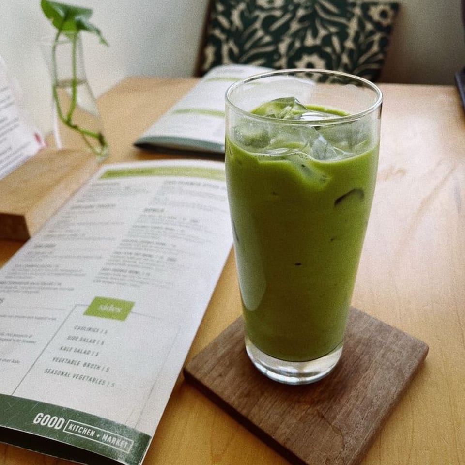 Iced green drink on a wooden coaster next to a Good Kitchen menu on a light wooden table.